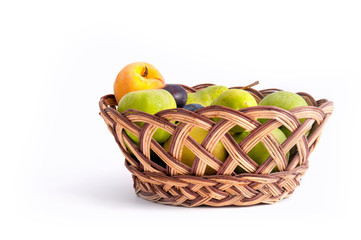 Apples, pears, plums, banana and peach in a wicker, brown basket on a light background. Fruit on a white background. Background of fruits.