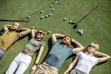 Fototapete Rund Group of a young and cheerful friends lying on the golf course with balls and putters on the grass, resting and having fun after the game © rh2010