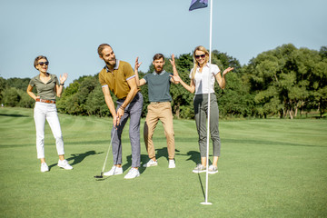 Group of a young friends practising golf together, scoring the ball with putter into the hole on...