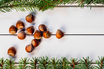 Christmas card with hazelnuts and fir branches on white wooden background
