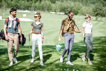 Young and elegant friends walking with golf equipment, hanging out together before the golf play on the beautiful course on a sunny day