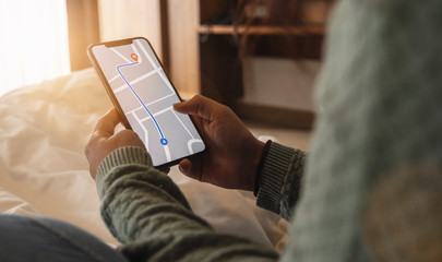 Tourist using GPS map navigation app on smartphone screen to get direction to destination address in the city at a hotel room, travel and technology concept image