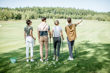 Young and elegant friends standing together with golf equipment during a golf play on the beautiful course on a sunny day