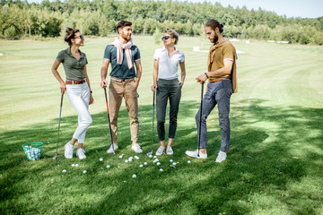 Young and elegant friends standing together with golf equipment during a golf play on the beautiful course on a sunny day