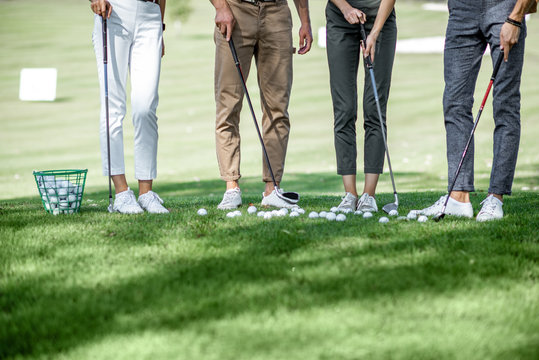 Friends standing together with golf equipment and balls on the green grass, cropped image with no face