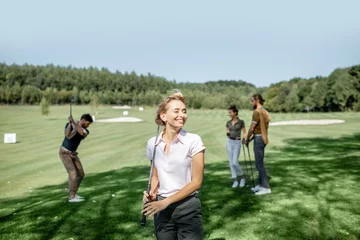 Stoff pro Meter Portrait of an elegant young woman standing with golf putter and friends playing golf on the background © rh2010