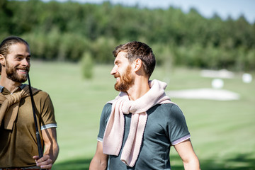 Fototapeta premium Two male best friends walking with golf equipment on beautiful playing course, talking and having fun during a game on a sunny day
