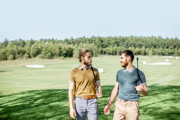 Two male best friends walking with golf equipment on beautiful playing course, talking and having fun during a game on a sunny day