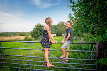 Brother and sister sitting on farm gate in the countryside