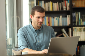 Serious adult man writing on laptop in a coffee shop