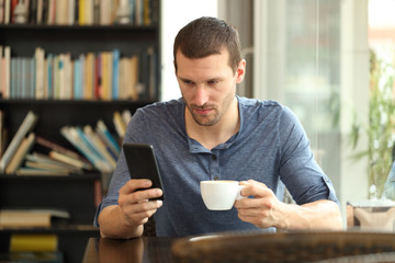 Serious man checking smart phone in a coffee shop