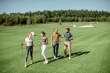 Group of friends talking and walking with putters during the golf play on the beautiful course on a sunny day