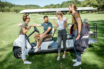 Group of a young friends hanging out together with golf equipment near the golf car on the playing course before the game