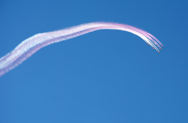 Aerobatic team flying in formation and leaving white pink smoke trail on blue sky