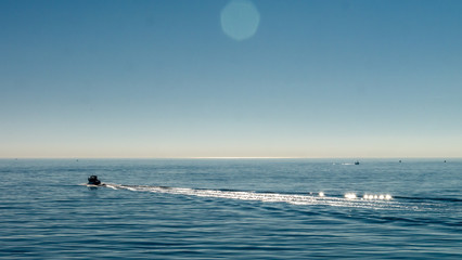 Small motor powered speed road creating waves in the North Sea, taken at Roker Pier, Sunderland, Tyne & Wear, England UK. Image with blue cloudless sky and calm, serene sea.