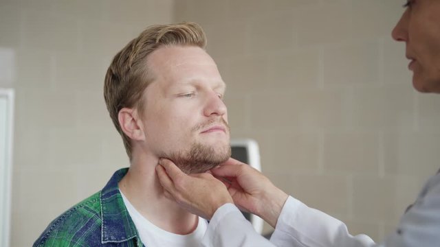 Closeup rack focus shot of female general practitioner checking tonsils of middle aged male patient and asking him questions about symptoms in doctors office