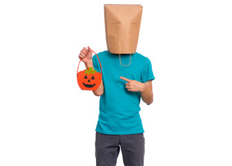 Happy halloween concept. Teen boy with paper bag over his head holds orange pumpkin bucket, isolated on white background. Portrait of teenager cover head with bag. Child waiting candy.