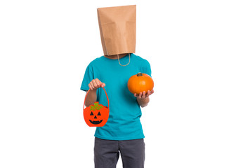 Happy halloween concept. Teen boy with paper bag over his head holds orange pumpkin bucket and small pumpkin, isolated on white background. Teenager cover head with bag. Child waiting candy.