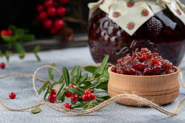 Lingonberry jam or sauce in wood bowl and in a glass jar with cranberries, cowberries on wood background