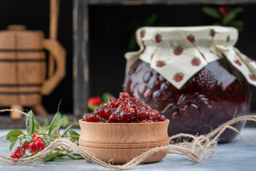 Lingonberry jam or sauce in wood bowl and in a glass jar with cranberries, cowberries on wood background