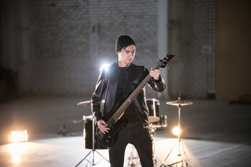 Fototapeta premium A musician man holding guitar and playing it on the background of a drum-kit