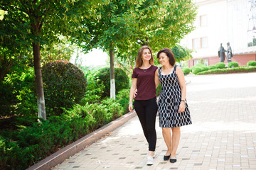 Mature mother hugging with her teen daughter outdoor in nature on sunny day.