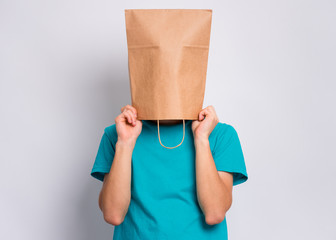 Portrait of teen boy with paper bag over head. Teenager cover head with bag holding hand near face posing in studio. Child pulling paper bag over head. - obrazy, fototapety, plakaty
