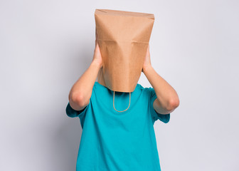 Portrait of teen boy with paper bag over head covering ears with his hands. Teenager cover head with bag closing ears with palms posing in studio. Child pulling bag over head. Hear no evil concept.