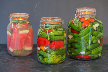 Preserves or pickled vegetables in glass jars. On the wooden black background.	