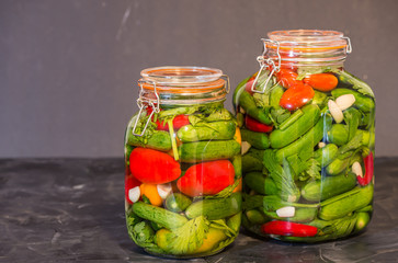 Preserves or pickled vegetables in glass jars. On the wooden black background.	