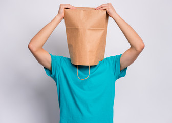 Portrait of surprised teen boy hold hands on head with paper bag over head. Teenager cover head with shopping bag, isolated on white background. Child with bag posing in studio.
