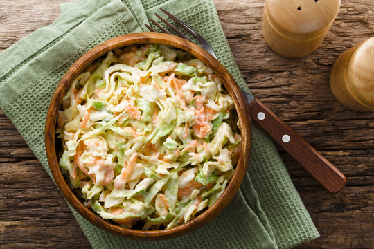 Coleslaw made of freshly shredded white cabbage and grated carrot with homemade mayonnaise-based salad dressing in wooden bowl, photographed overhead (Selective Focus, Focus on the salad)