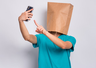 Teen boy with paper bag over head make selfie by mobile phone, isolated on white background....