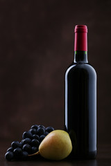 Fototapeta premium Bottle of wine with grapes and pear on brown background