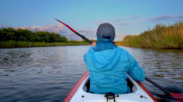 A woman is kayaking on a calm river. She is rowing with oars. Slow motion
