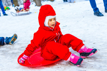 Pretty smiling little girl in her ski suit sliding down a small snow covered hill with her sledge