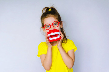 Little funny girl kid with toothbrush, dental mockup (jaw), red glasses in hand. Concept of health, oral hygiene, people and beauty. Space for your text. Selective focus.