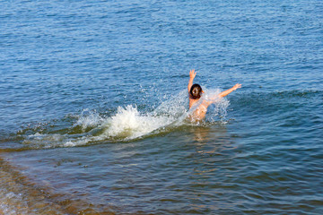 The boy runs and jumps into the sea water.