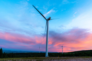 wind turbine at sunset with red clouds on horizon and blue sky.