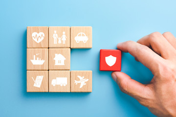 Hand holding red wooden blocks with insurance icons. family, life, car, travel, health and house insurance icons, blue background, Insurance concept - obrazy, fototapety, plakaty