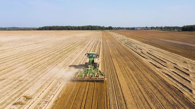 Tractor pulls a disc harrow system implement to smooth over a dirt field in preparation for planting