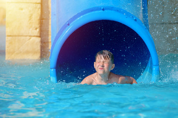 Young boy or kid has fun splashing into pool after going down water slide during summer