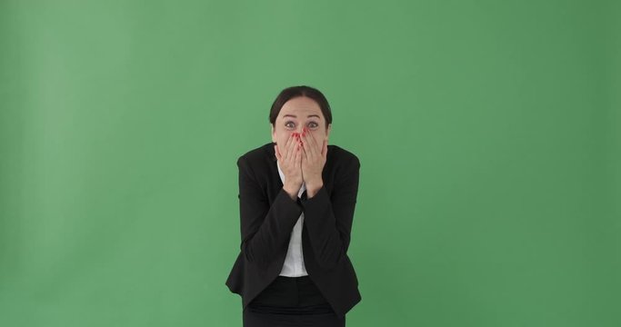 Surprised businesswoman covering mouth with hands over green background