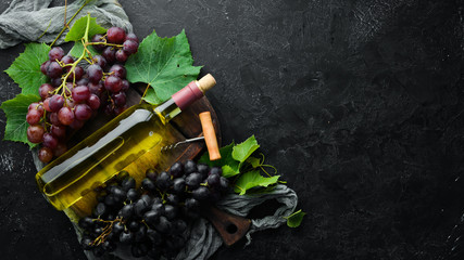 Bottle of white wine and fresh grapes on a black stone table. Top view. Free space for your text.