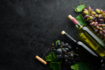 Bottle of red and white wine and grapes on a black stone table. Top view. Free space for your text.
