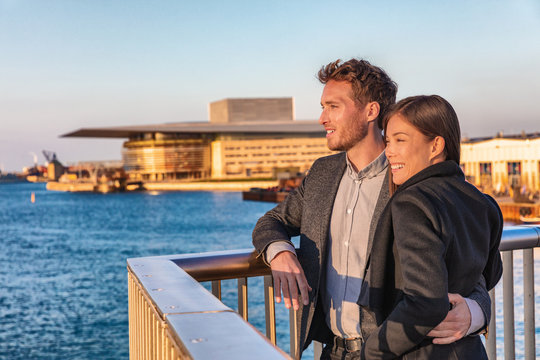Europe travel tourists couple enjoying sunset view at Copenhagen harbourfront by the Opera, Denmark european holiday lifestyle. Asian woman, Danish man interracial people.
