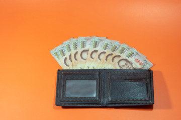 One thousand baht Thai banknotes in a black purse on an orange background