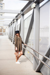 Fashion female model dressed casual in a grungy location. Fashion blogger in military shirt and hat on a pedestrian bridge