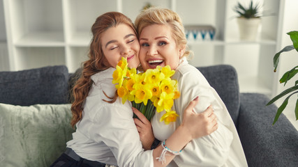 Laughing grandmother and granddaughter cuddling and holding flowers