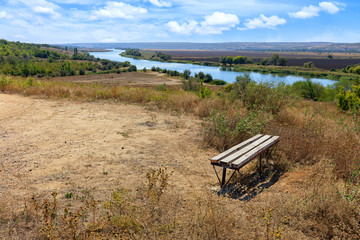 View of a wooden bench on a high river bank on a bright autumn day. Rural autumn landscape.